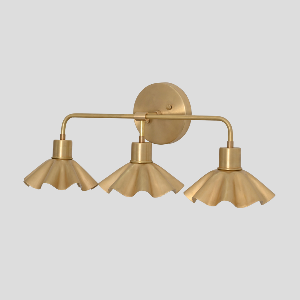 Tripe brass vanity light with flower shaped shade on a gray background