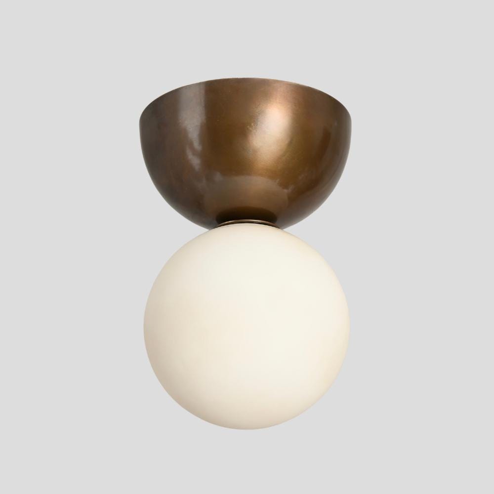 A minimalistic flush mount ceiling light with an antique brass finish and a white glass globe.
