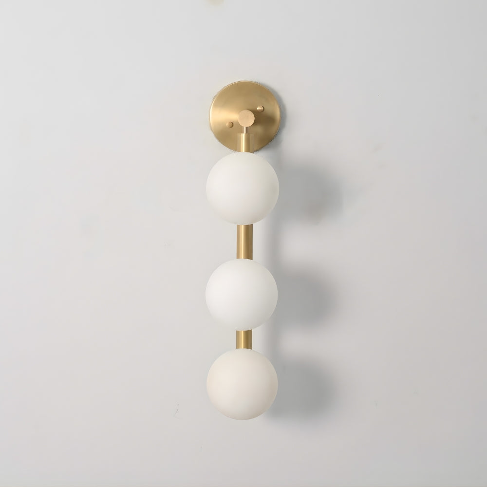 Wall sconce with 3 white glass globe and raw brass accents on a light gray background