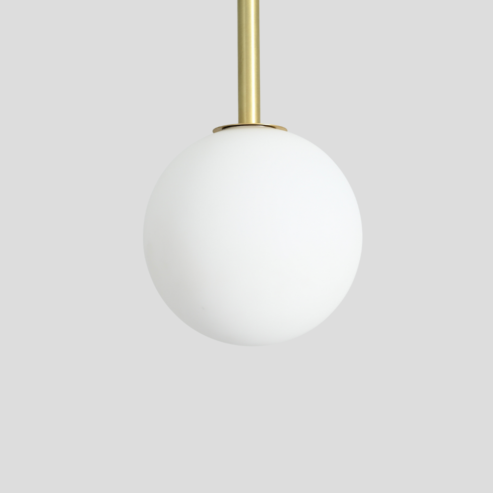 Close up on the opal glass globe of a brass vertical pendant on a gray wall