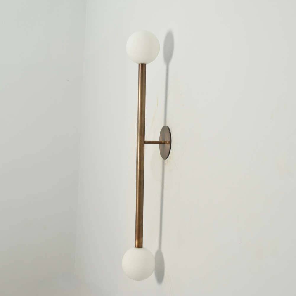 Wall-mounted light fixture with a brass spherical shade and a double frosted glass globe on a plain background