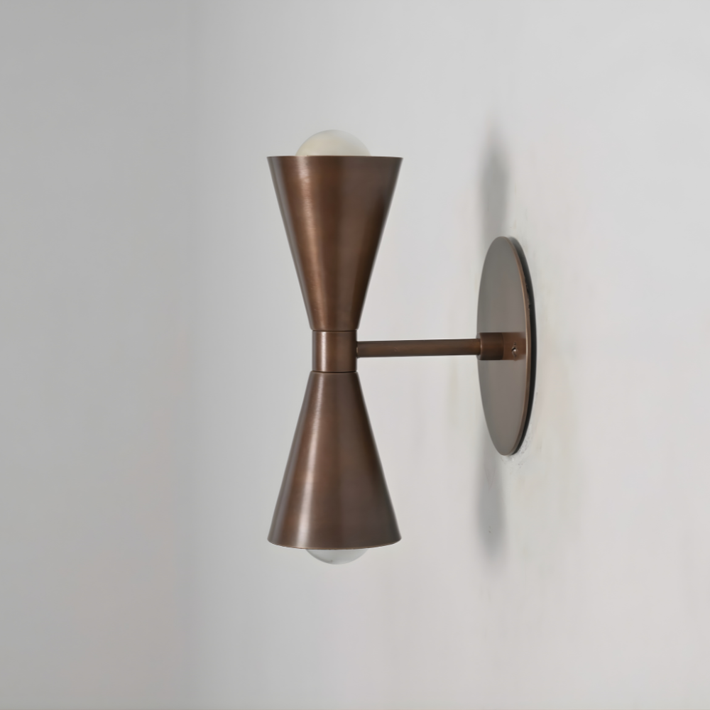Dual cone wall lamp handcrafted in apure antique brass finish on a gray wall by LightCove