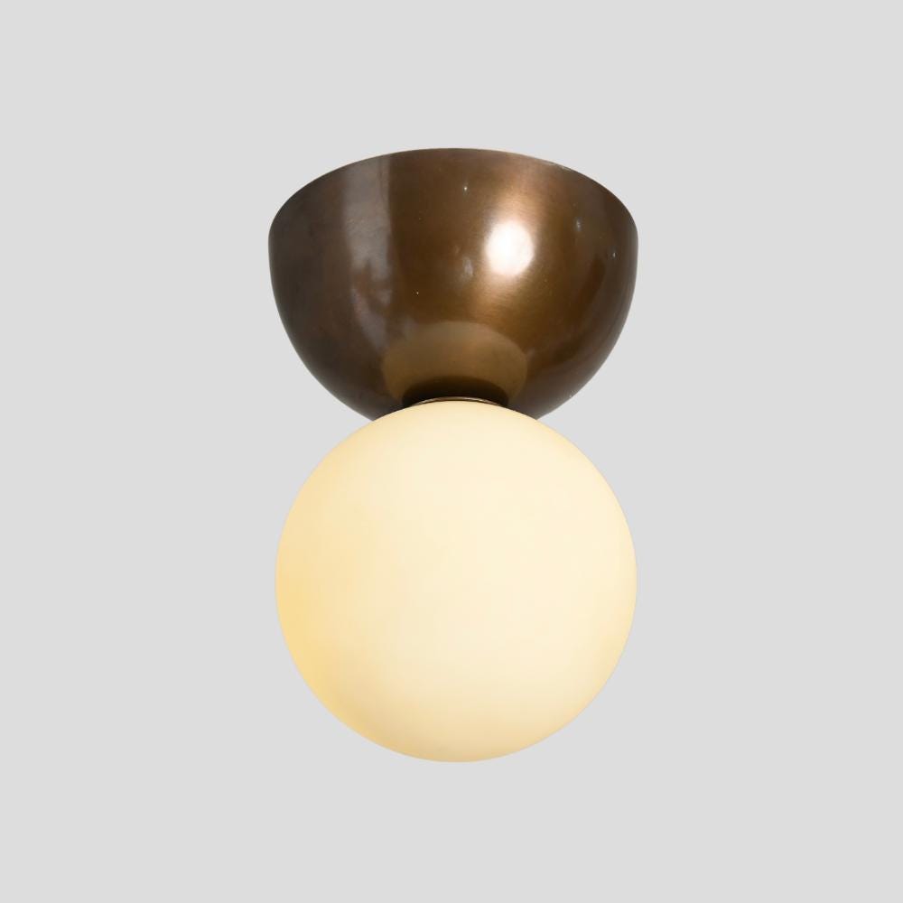 A minimalistic brass flush mount with a glass globe orb pendant on gray background by lightcove