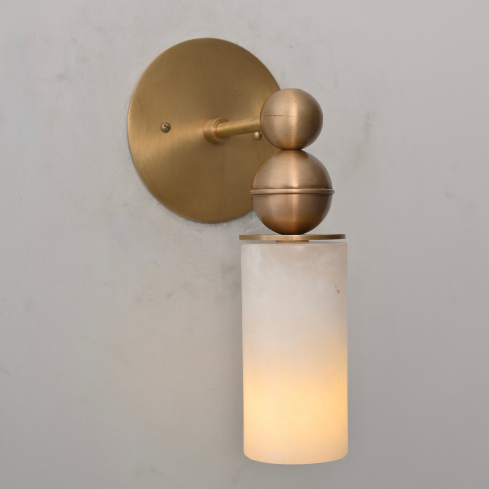 Brass wall sconce with cylindrical glass shade on a neutral background