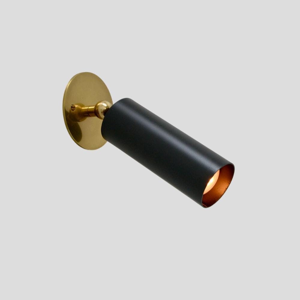 A brass cylinder wall sconce with a minimalistic black finish and a gold-colored cap.