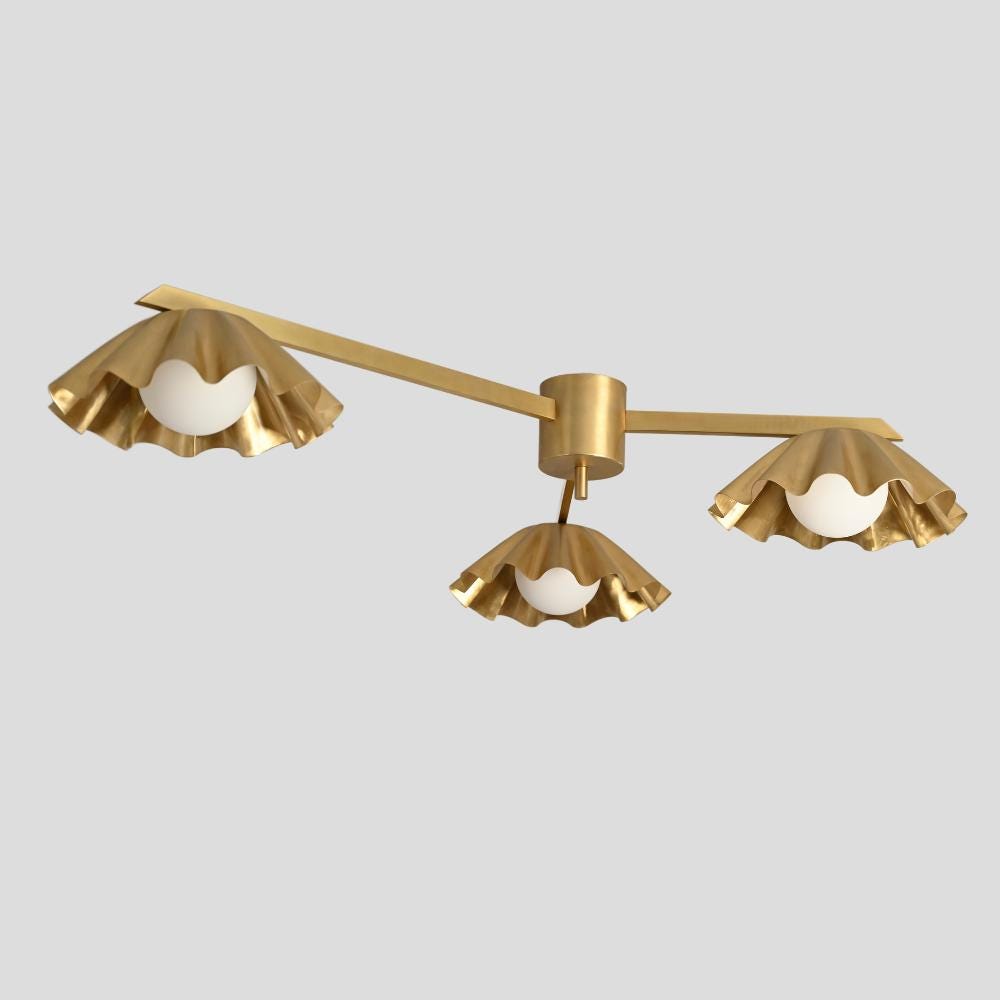 A ceiling-mounted three-arm flush mount light with a raw brass finish and handmade glass globe, designed in a mid-century modern style.