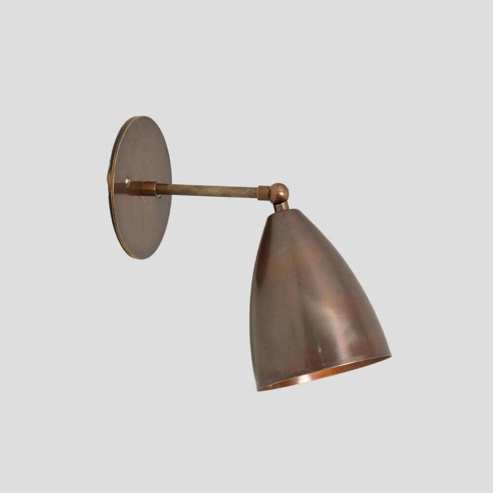 Antique brass wall sconce with an adjustable shade, showing a metallic finish and a conical light cover.