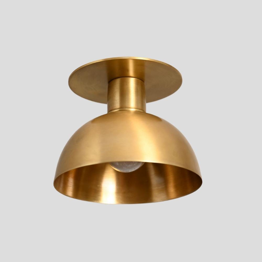A semi flush mount ceiling light with a brass finish and a visible light bulb inside, designed in a mid-century modern style.