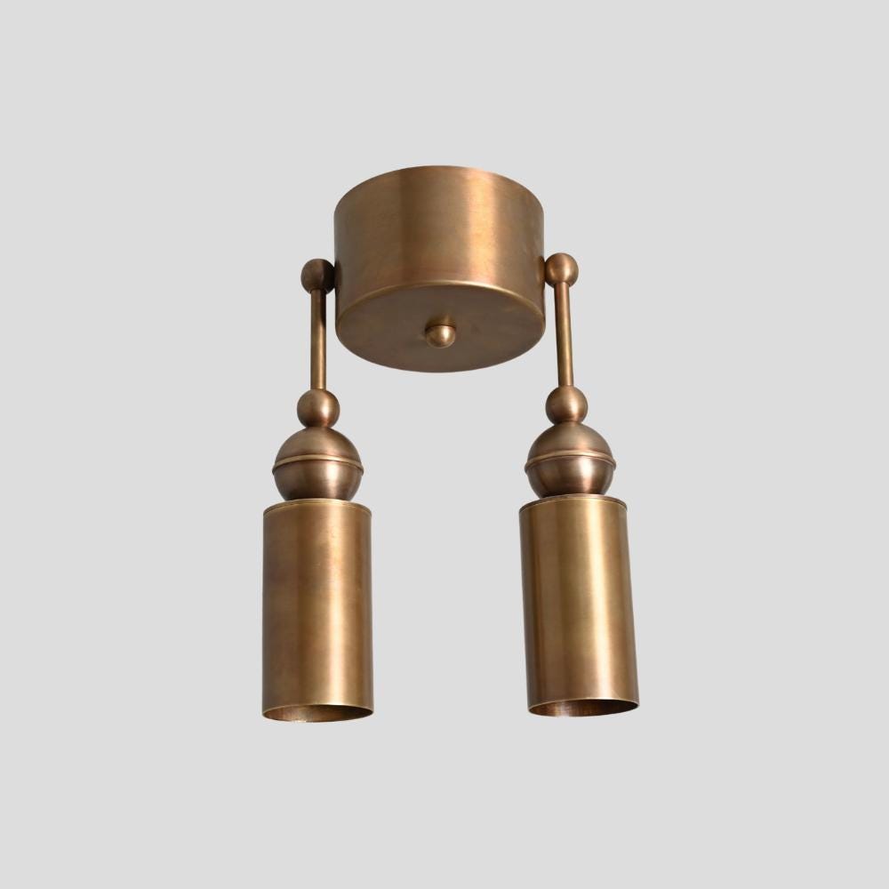 A brass wall sconce with a cylindrical shape, featuring a double ceiling light design with two extendable arms, against a white background.