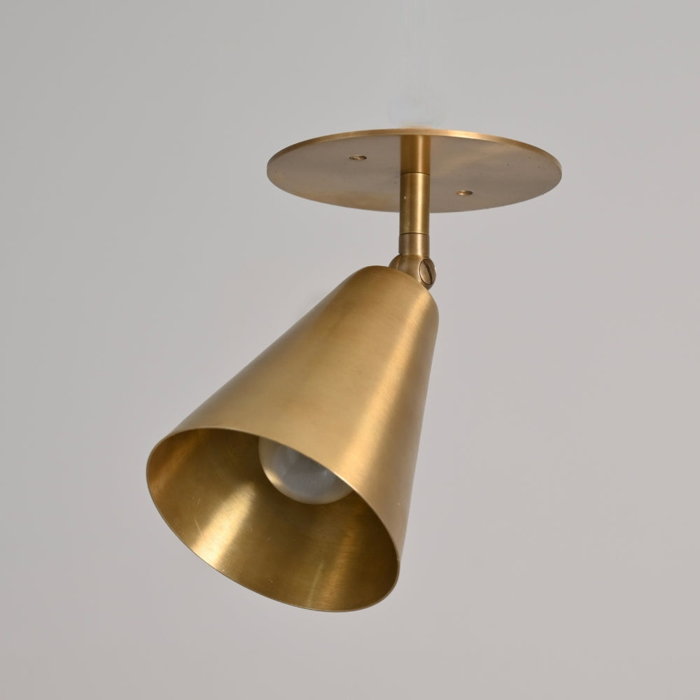 Modern directional brass cone wall lamp on a gray wall.