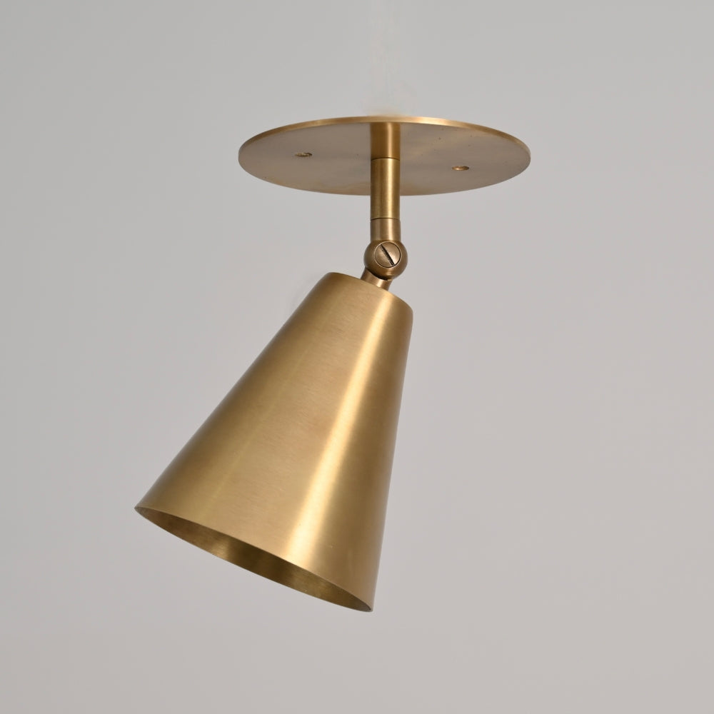 Modern mid century brass ceiling spot light with an adjustable shade on a gray wall.