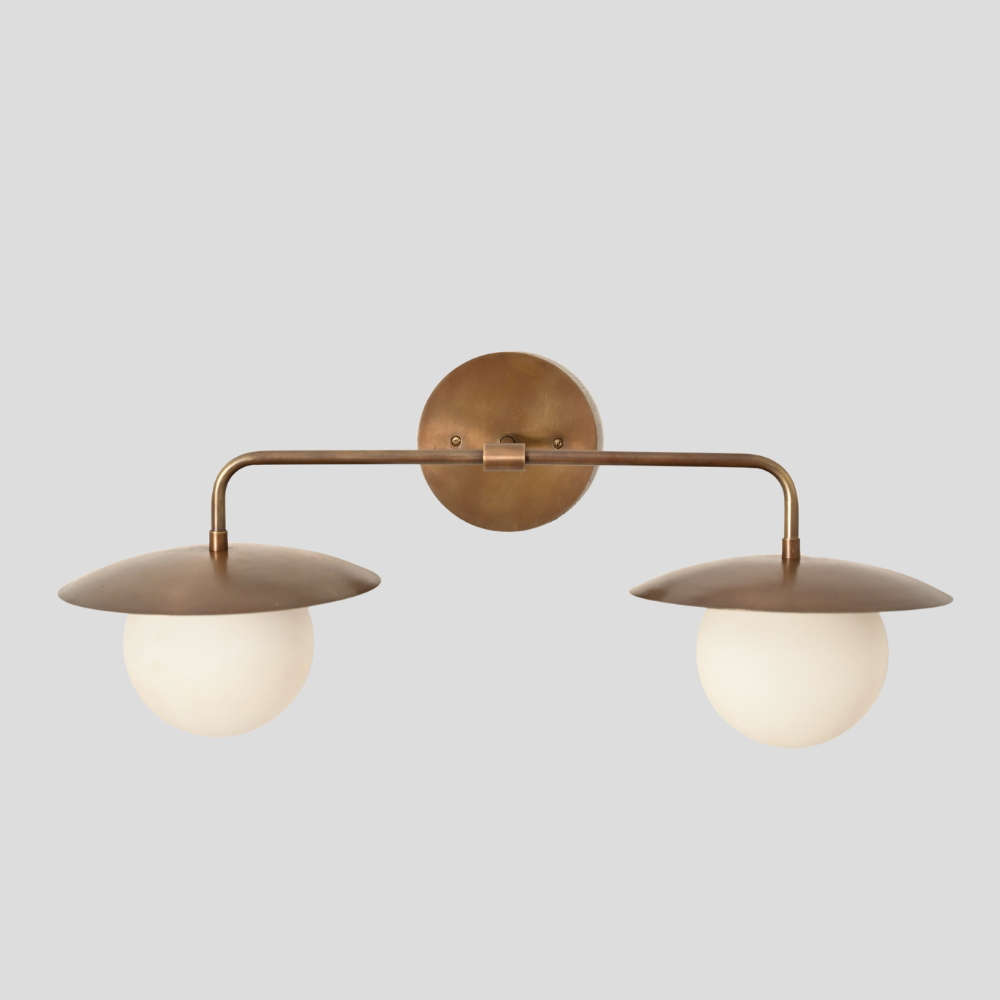 Brass wall-mounted light fixture with two round glass shades on a gray background