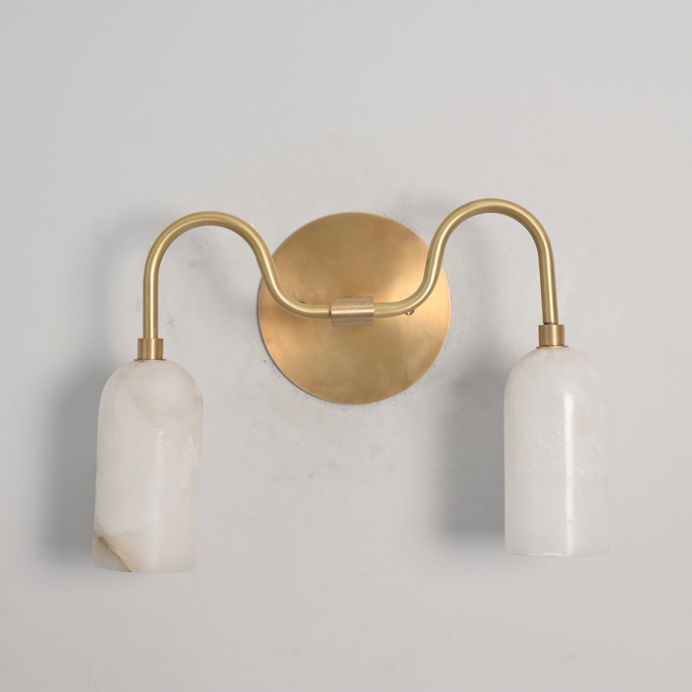 Dual alabaster wall sconce with curved brass arm mounted on white wall