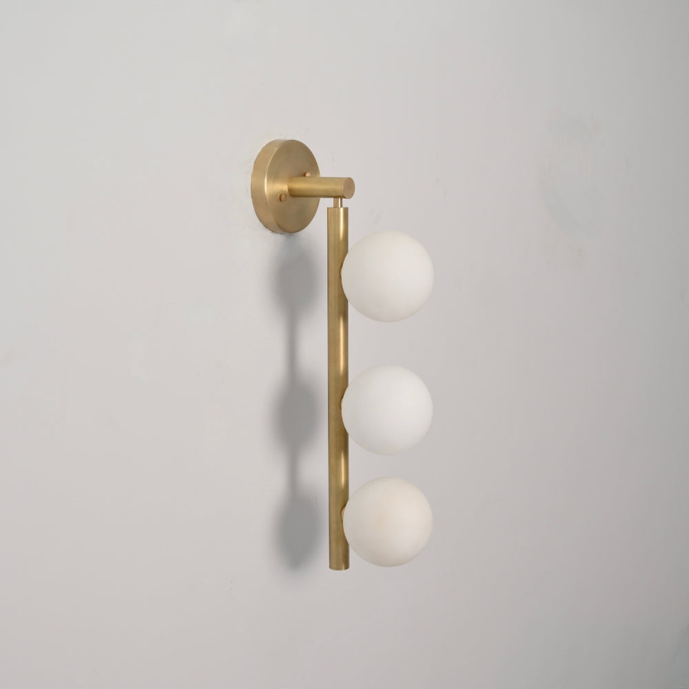 Brass wall lamp  with brass finish and three frosted glass spheres on a gray background