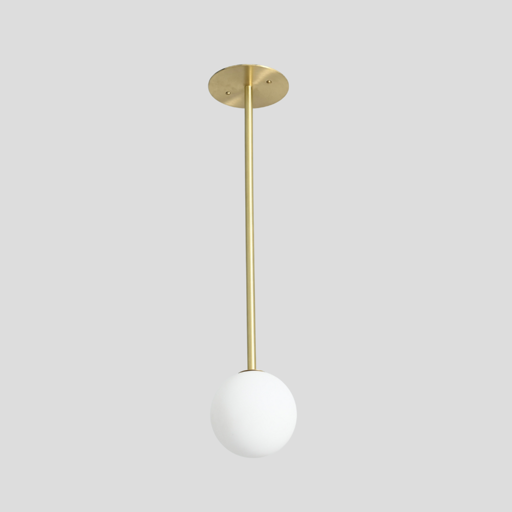 handmade brass vertical ceiling light with a single frosted glass globe on a gray background