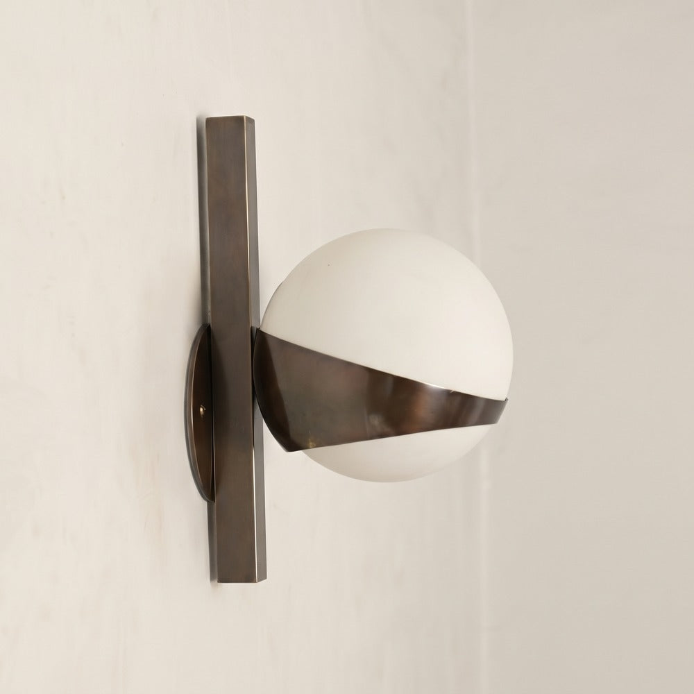 Opal glass globe wall light cradled by a curved brass band, three-quarter view