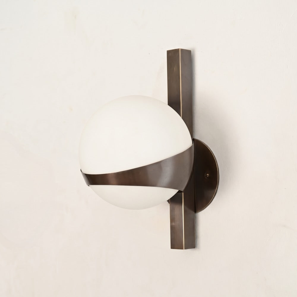 Minimalist brass wall sconce with frosted opal globe mounted on a vertical brass bar