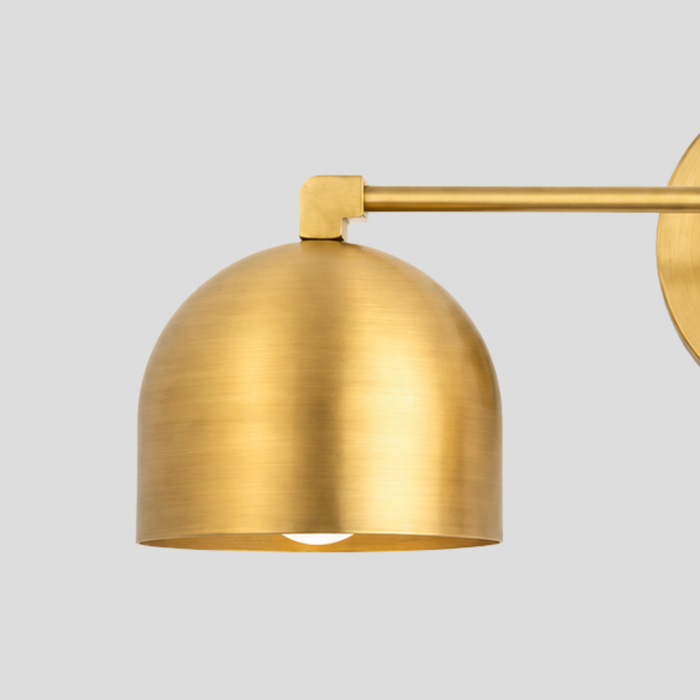Close-up of a Double Brass Dome Vanity Light - Mid Century Linear Wall Sconce, highlighting the textured raw brass finish on the curved dome shade and horizontal connecting rod.