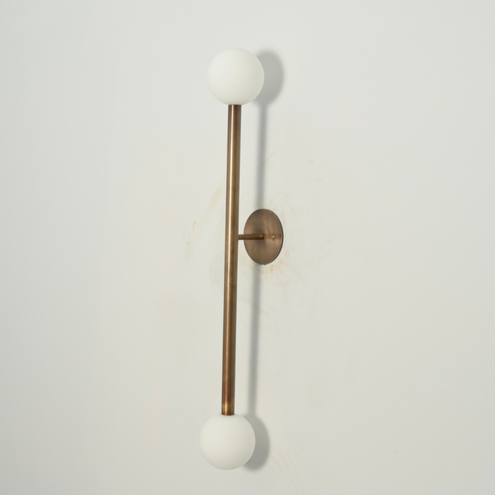 Vertical arm brass globe wall sconce in a mid century design on a gray background