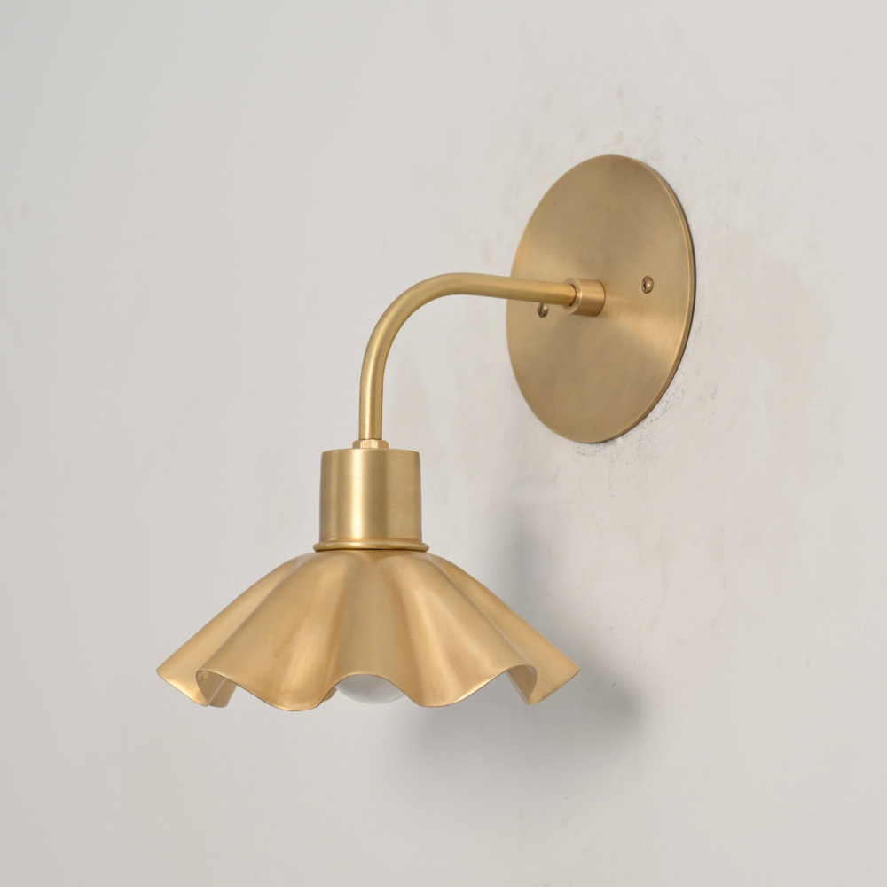 Minimalist brass wall sconce with a flower shaped shade on a gray wall designed by LightCove 