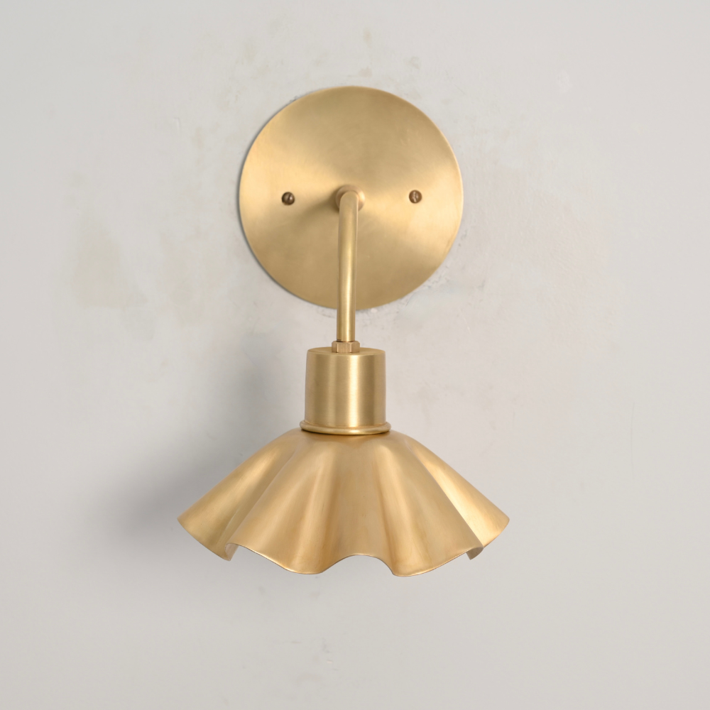 Minimalist brass flower shaped shade wall lamp with a clean curved rod on a gray wall 