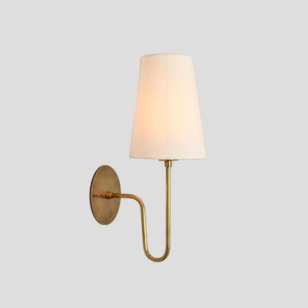 A wall-mounted antique brass sconce with a linen shade, designed for vanity or bedside lighting.