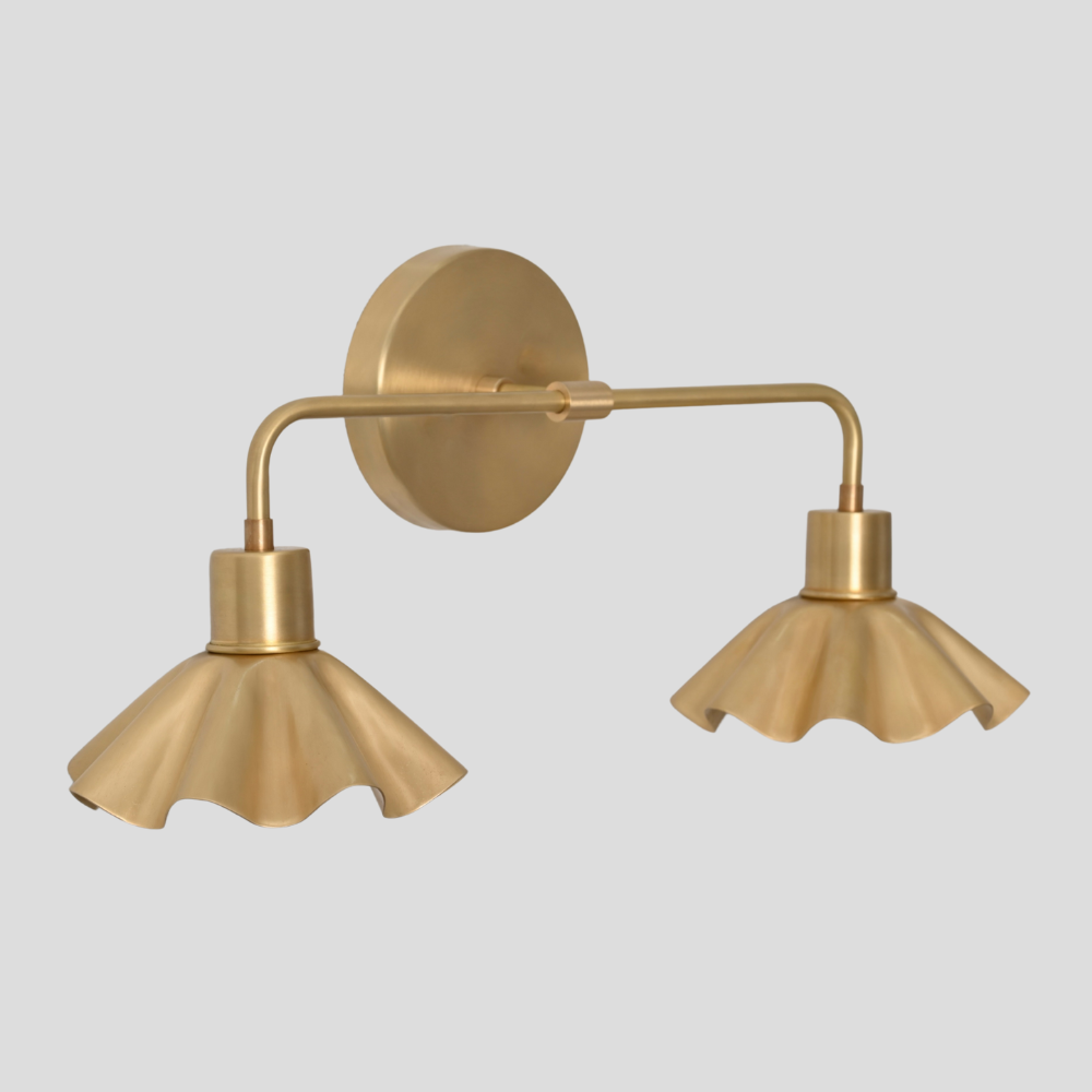 A raw brass vanity light with a double flower shade on a gray background