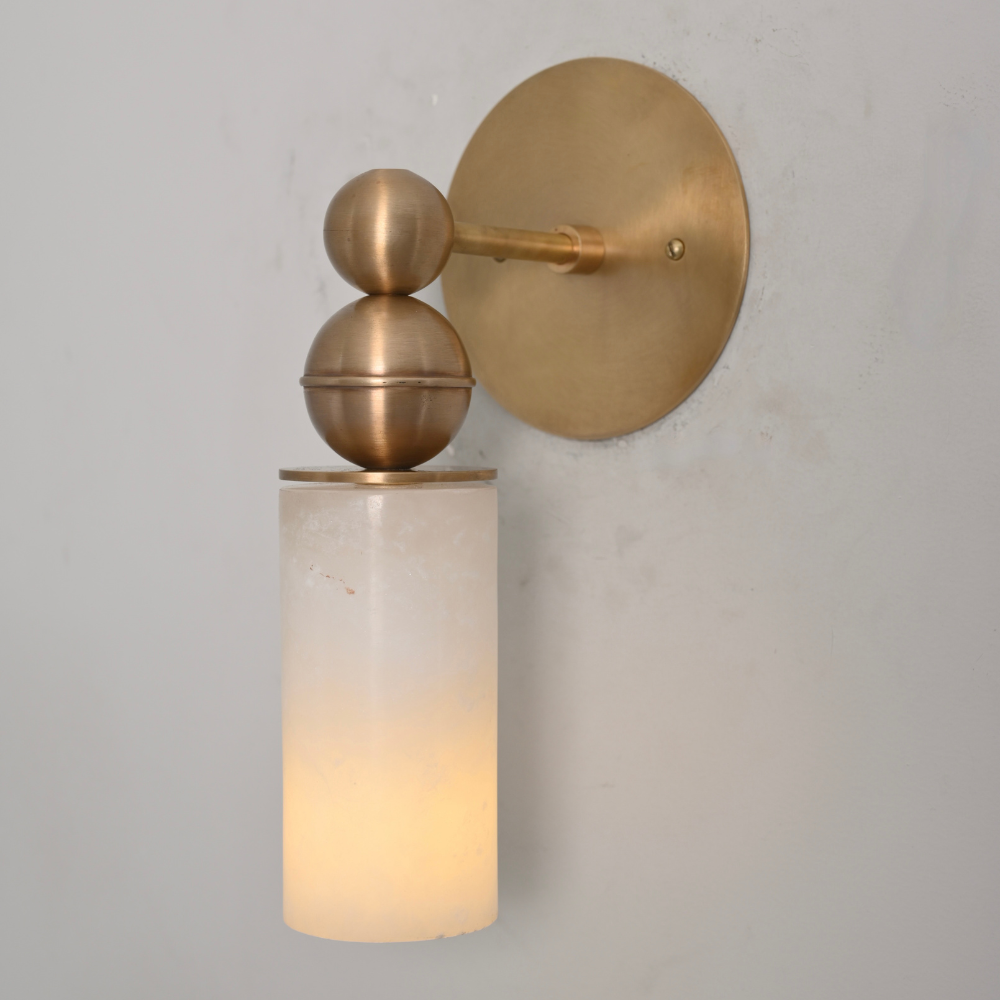 Brass wall sconce with a cylindrical glass shade on a gray background
