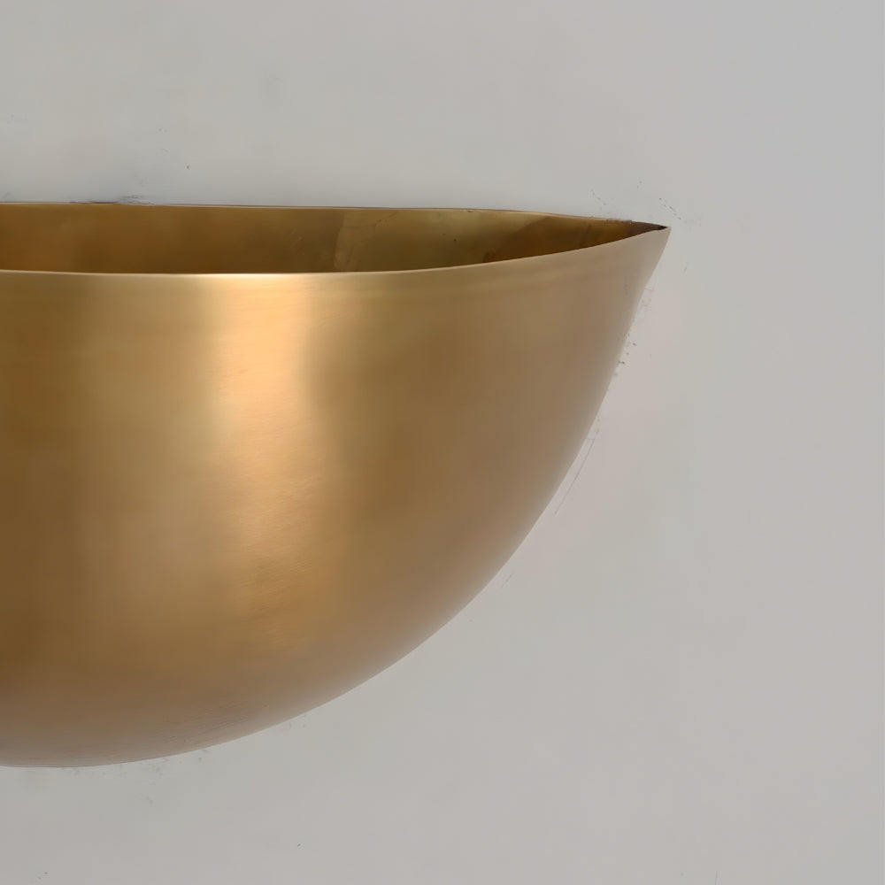 close up on the raw brass finish of an half moon shade wall light on a gray wall 